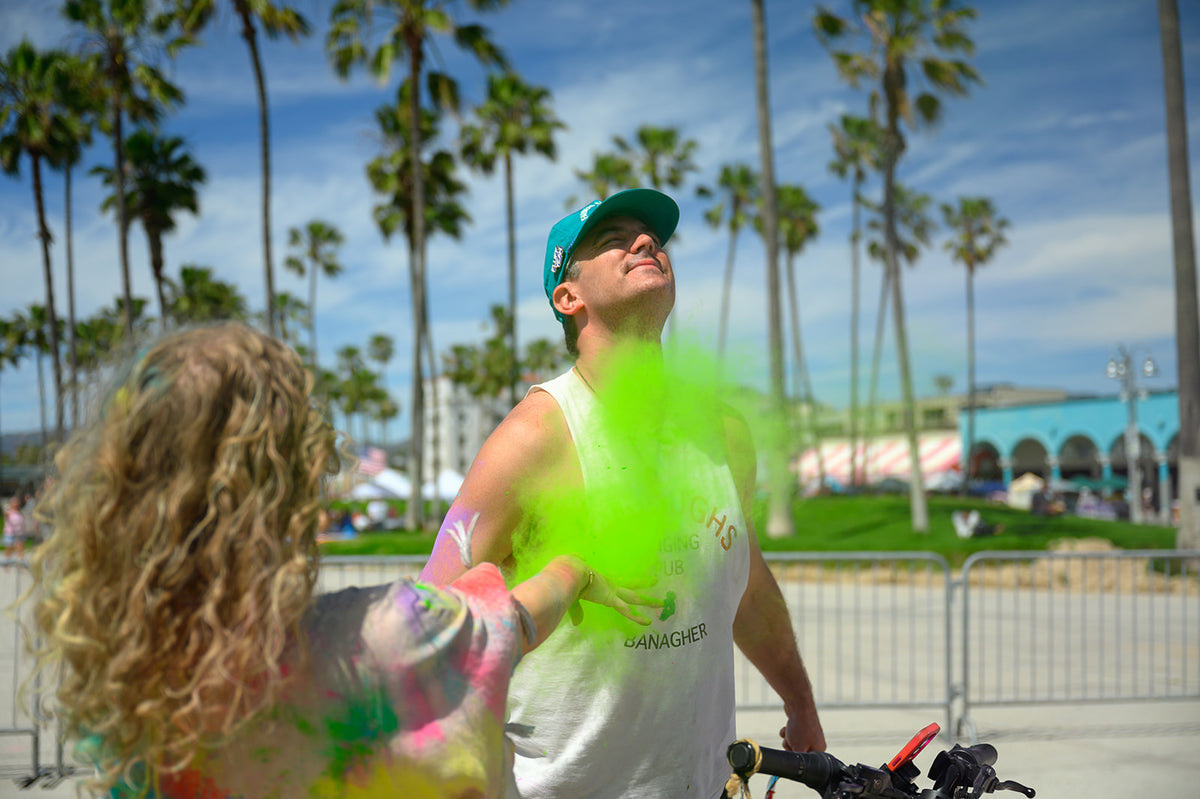 Green color powder thrown at a smiling man at an outdoor color party under palm trees